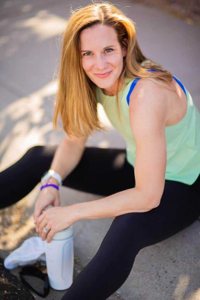Image of a fit woman sitting on the ground after a run, holding a water bottle, representing personalized running coaching services.