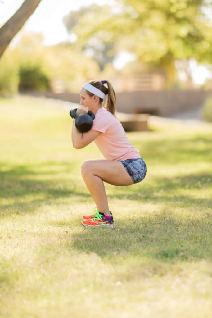 Woman doing squat with kettlebell outdoors for fitness training and strength building.