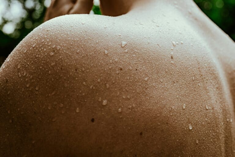 Close-up of a person's shoulder with water droplets, emphasizing hydration and skincare for runners.