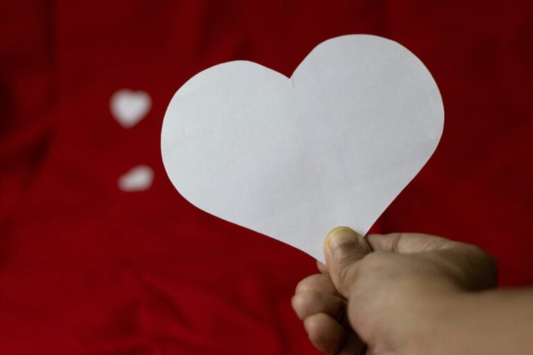 Heart-shaped paper note, symbolizing love, motivation, or care, held in hand against a vibrant red background.