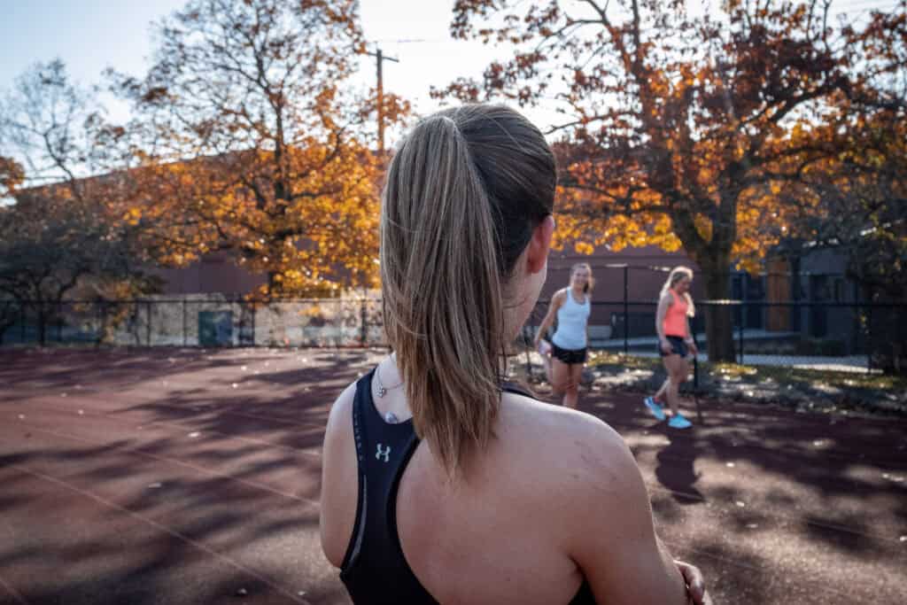 Athletic woman observing her running training session with teammates on outdoor tennis court during fall.