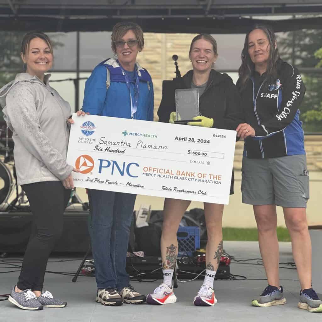 Female marathon winner with trophy and large check from Mercy Health.