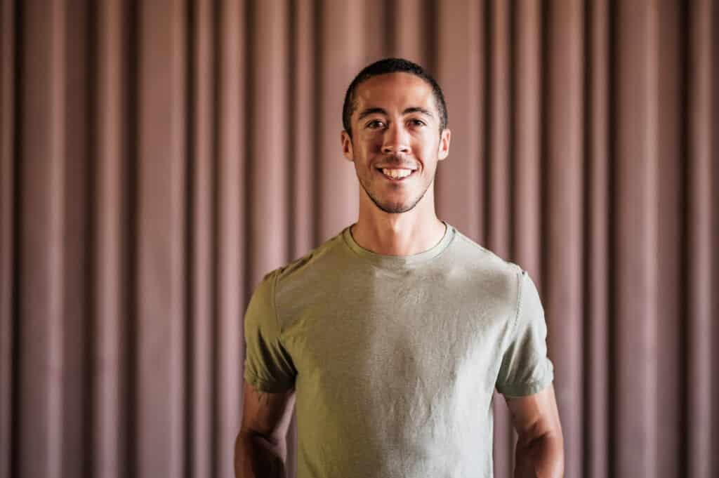 A smiling male runner poses indoors, promoting tailored running training and coaching services for beginners and advanced athletes.