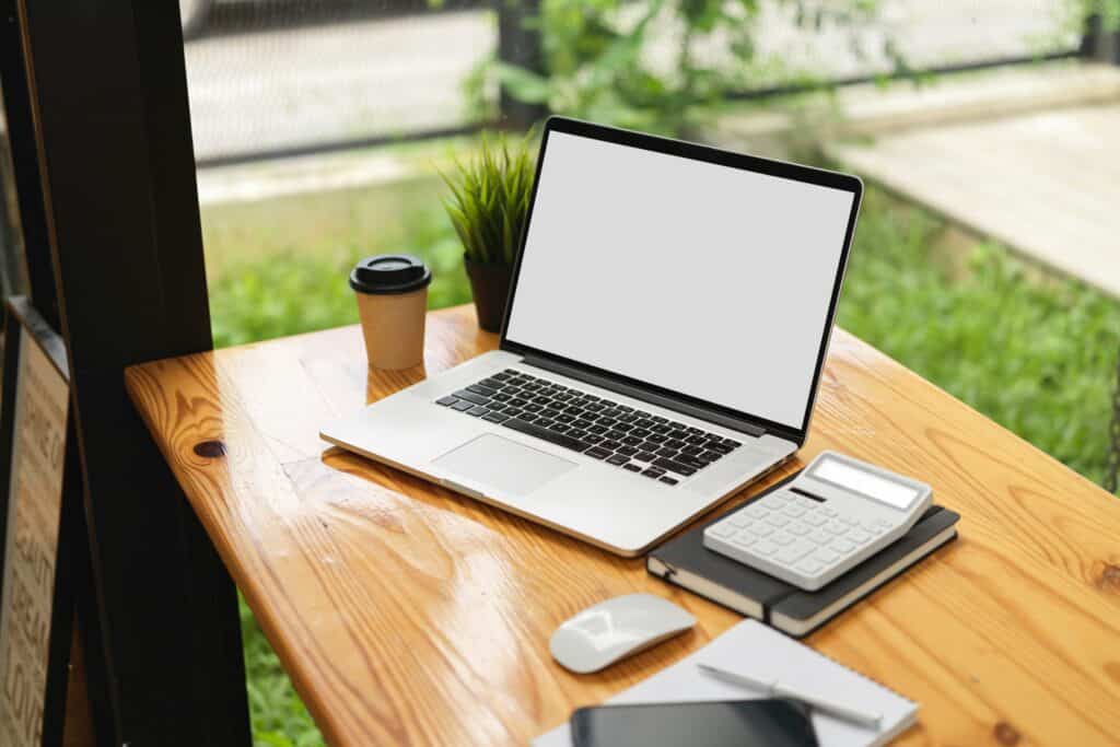 Laptop on wooden desk with calculator.