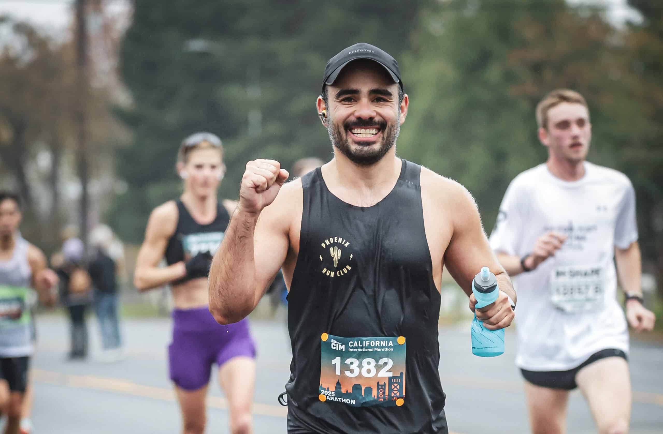 A happy runner in a marathon race wearing a black tank top and holding a water bottle, showcasing dedication and fitness.